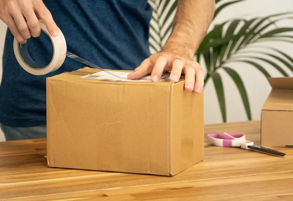 Osoba lijepi dostavnu naljepnicu na kartonski paket.