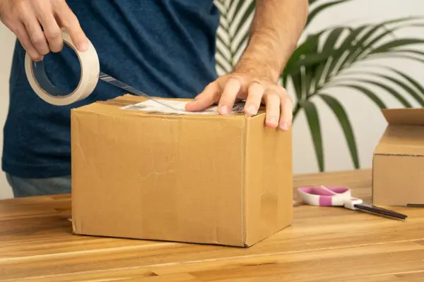 Osoba lijepi dostavnu naljepnicu na kartonski paket.
